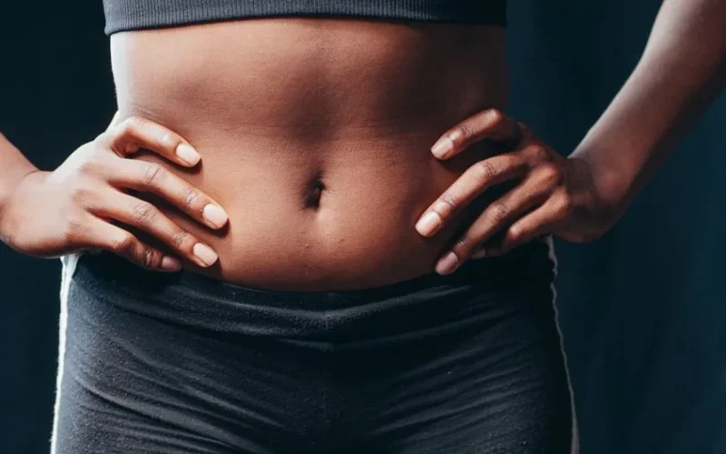 A close-up of a woman's toned midsection with hands on hips, showcasing fitness and health.