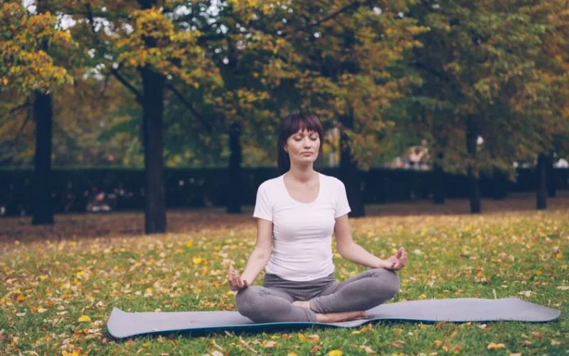 Serene woman practicing yoga in a park during autumn.