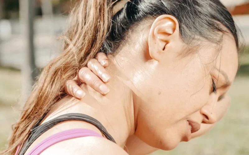 Close-up of a woman holding her neck, showing discomfort and pain outdoors.
