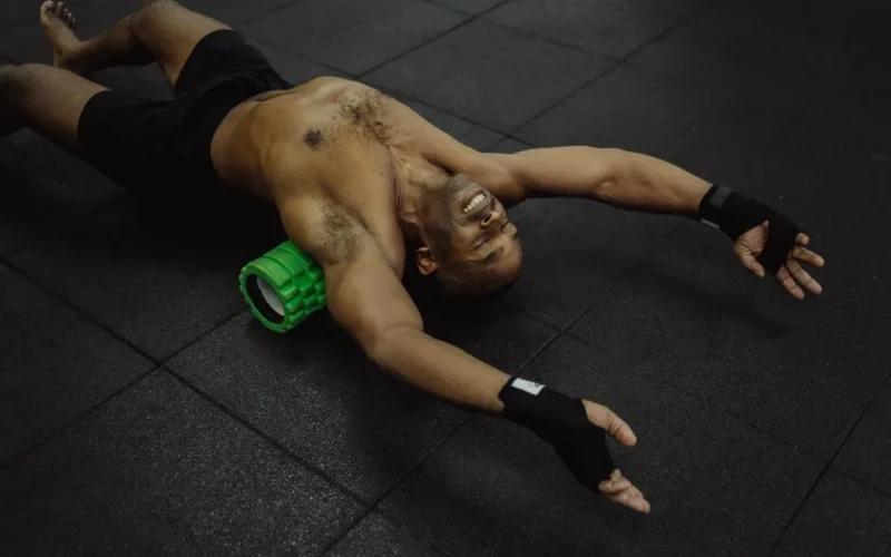 Shirtless man exercising with a foam roller in a fitness center.