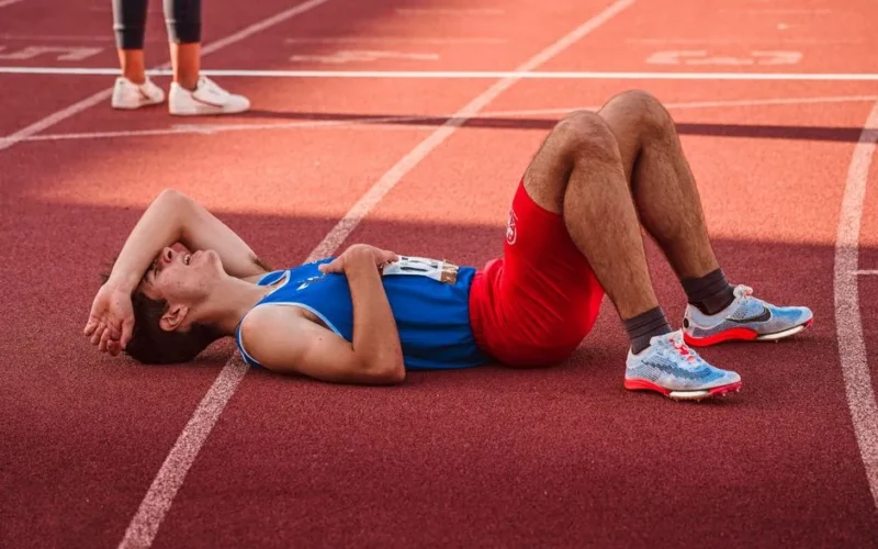 A tired athlete lies on the track, recovering after a race in sportswear.