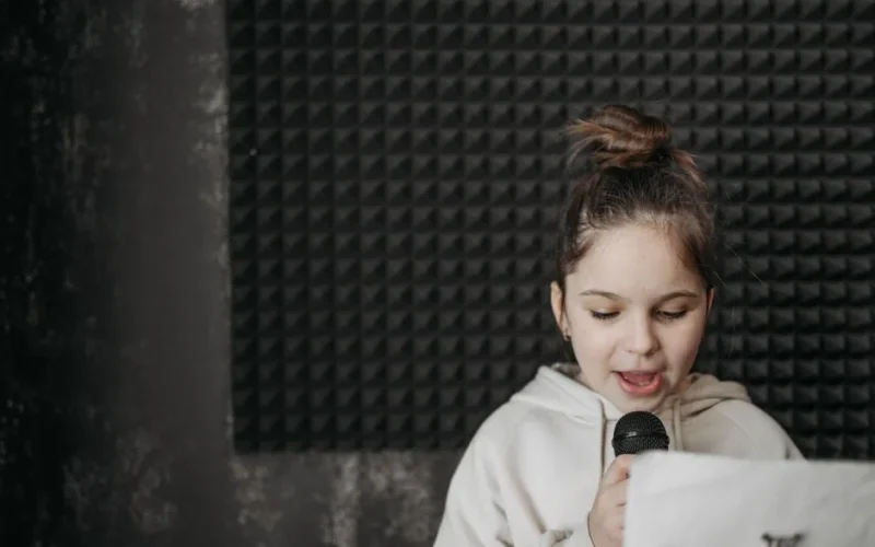 A young girl singing into a microphone in a soundproof recording studio.