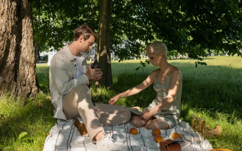 A couple enjoys a relaxing picnic on a blanket under trees in a sunlit park.