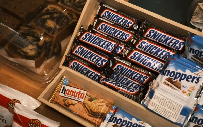A variety of chocolate and wafer snacks including Snickers and Hanuta in a wooden box.