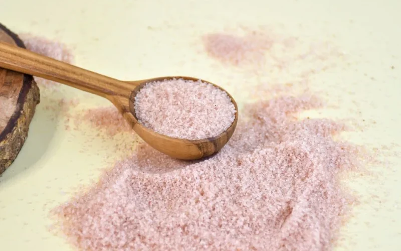 Close-up of pink Himalayan salt in a wooden spoon on a yellow background, highlighting texture.