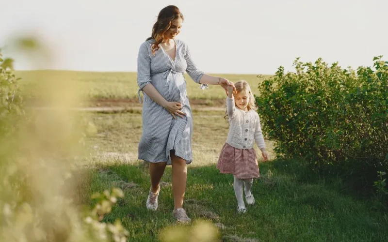 A pregnant mother enjoying a summer walk with her daughter in a green field.