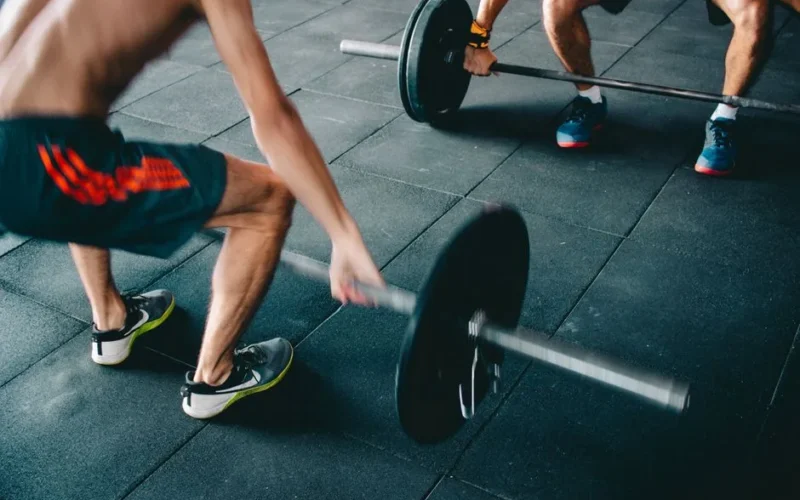 Two men lifting barbells showing strength and effort in a gym setting.