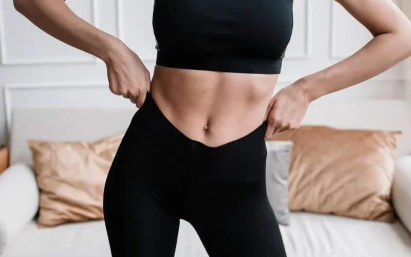 Close-up of a woman in activewear adjusting her pants in a stylish living room.