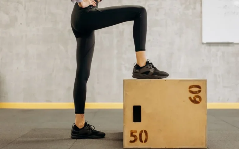 Female athlete performing workout in gym with wooden step box, showcasing fitness and balance.