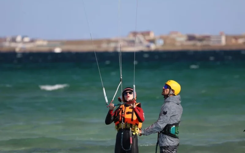 Instructor guiding kitesurfing lesson on a sunny day at the seaside. Safety gear emphasized.