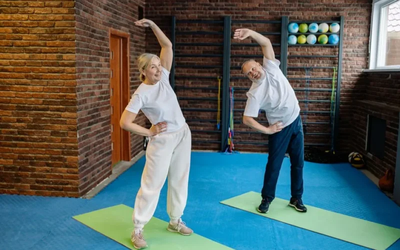 Elderly couple stretching on yoga mats in a home gym, embracing a healthy lifestyle.