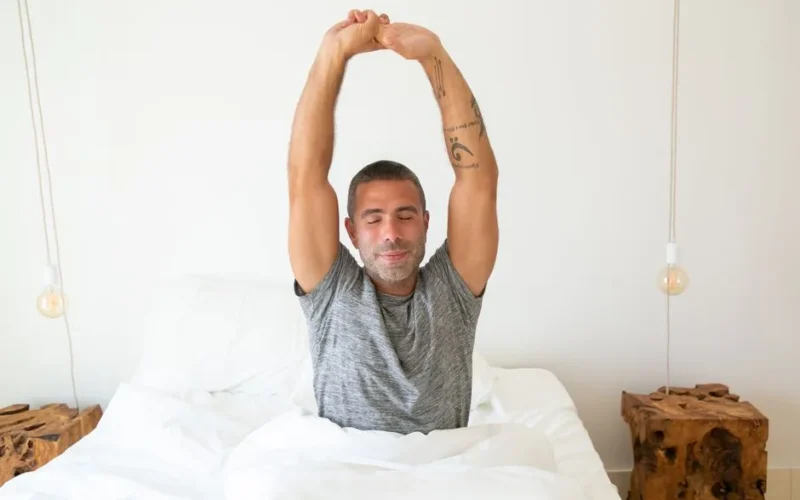 A man stretching his arms while waking up in bed, starting the morning with energy.