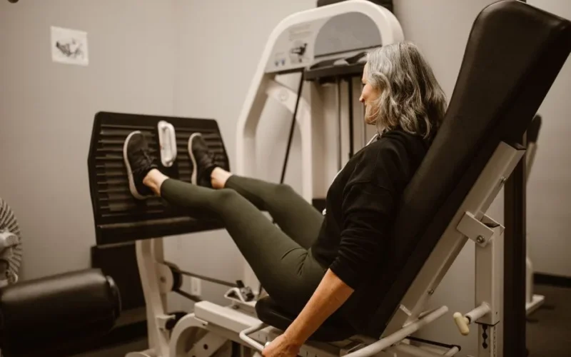 Mature woman working out on a leg press machine in a gym, promoting active and healthy lifestyle.