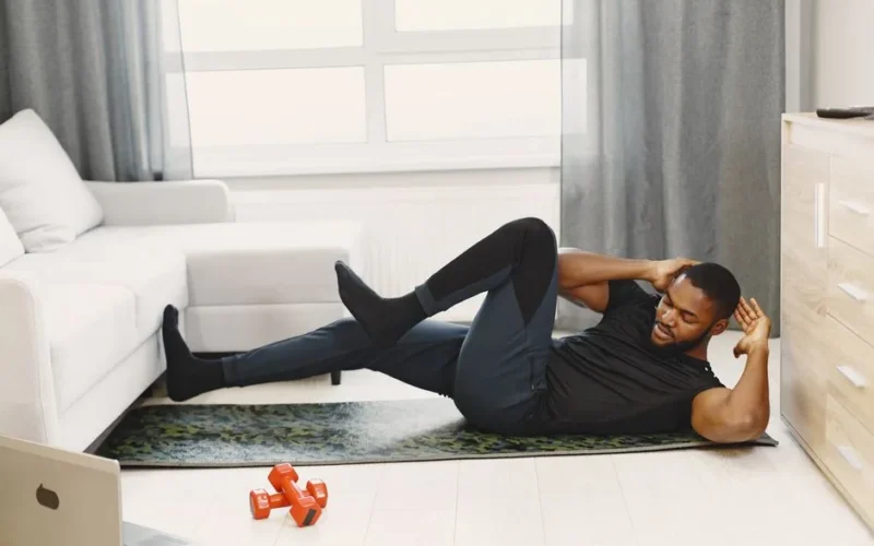 A black man performing abdominal exercises on a yoga mat at home.