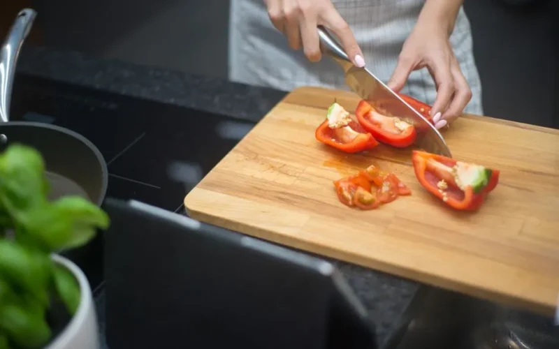 Close-up of a woman slicing red bell pepper in a modern kitchen setting.
