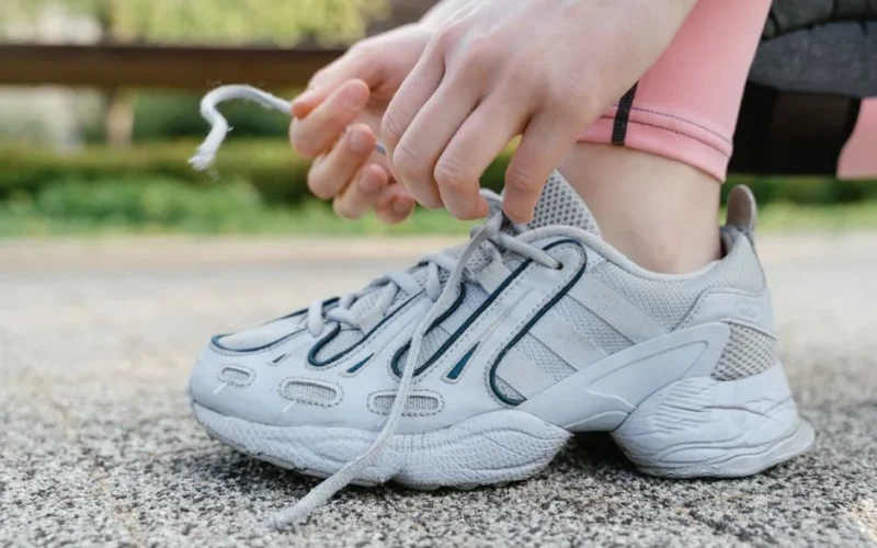 Close-up of a woman tying shoelaces on white sneakers during an outdoor exercise session.