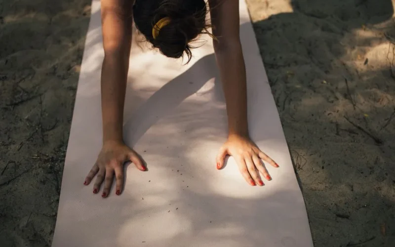 A woman exercises on a yoga mat in outdoor sunlight, promoting fitness and relaxation.