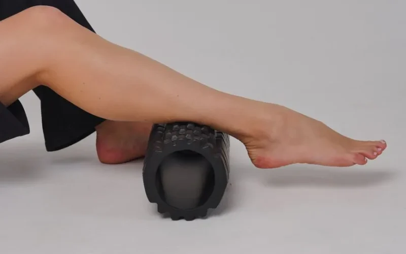 Close-up of a leg using a foam roller for stretching and muscle relief in a studio setting.