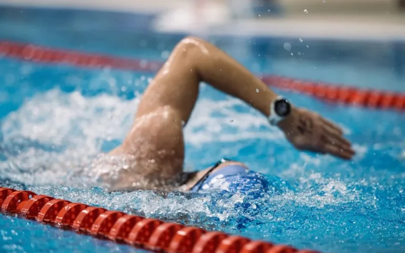 A focused swimmer performs a freestyle stroke in a competition-grade indoor pool.