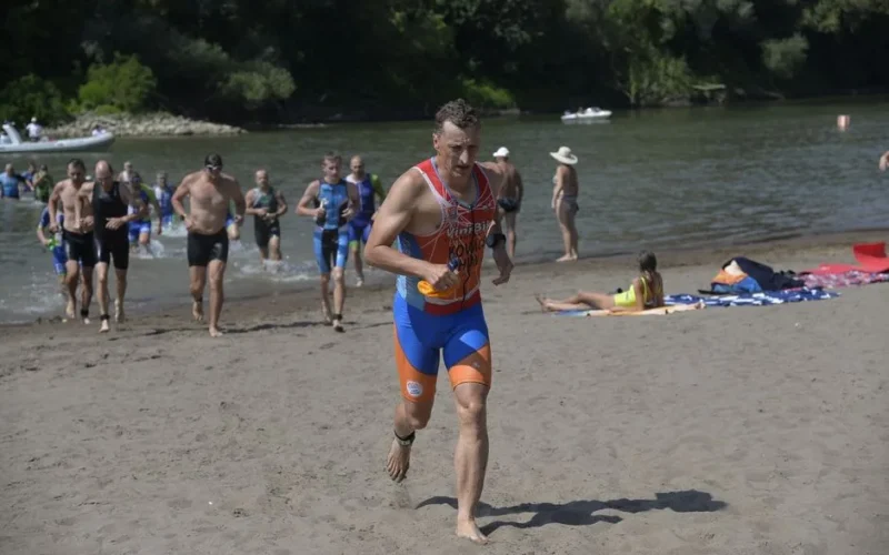 Action shot of triathletes transitioning from swim to run along Jánd riverbank.