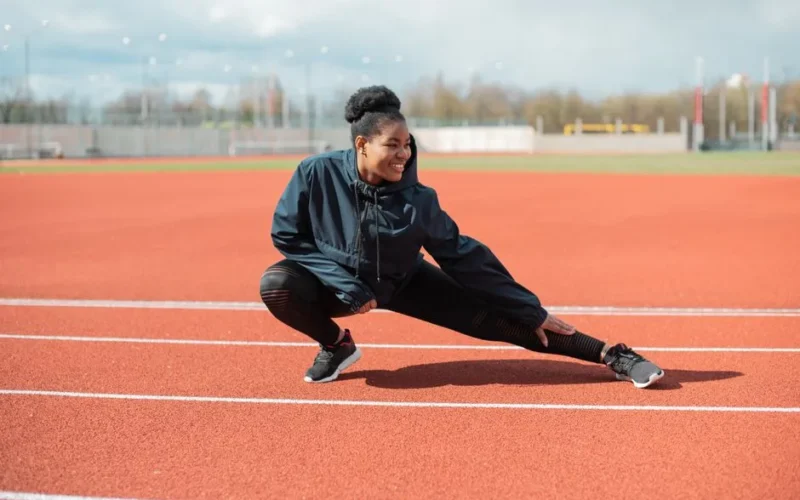 A woman in activewear stretches on a red running track outdoors, preparing for a workout.