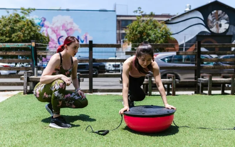 Two women exercising with a balance board outdoors. Fitness and teamwork in action.
