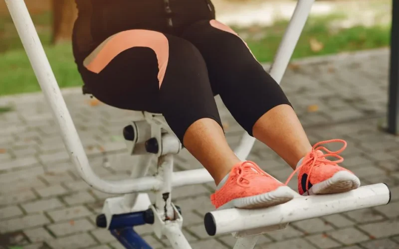 Close-up of a woman exercising on a fitness machine outdoors, focusing on her legs and shoes.