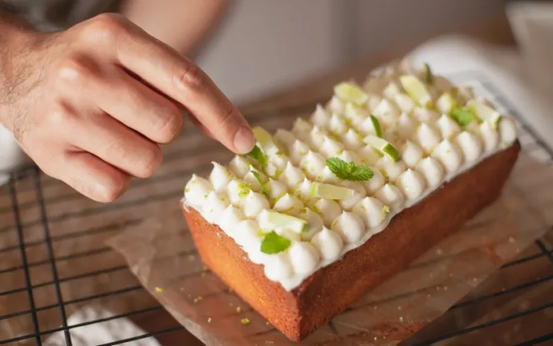 Tasty frosted cake with mint leaves being decorated by hand on a cooling rack.