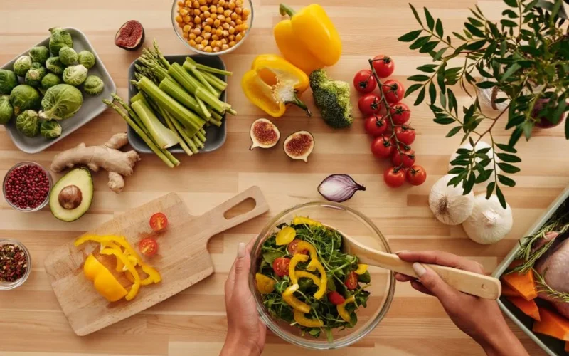 Top view of fresh vegetables and salad preparation on a wooden table, perfect for healthy eating concepts.