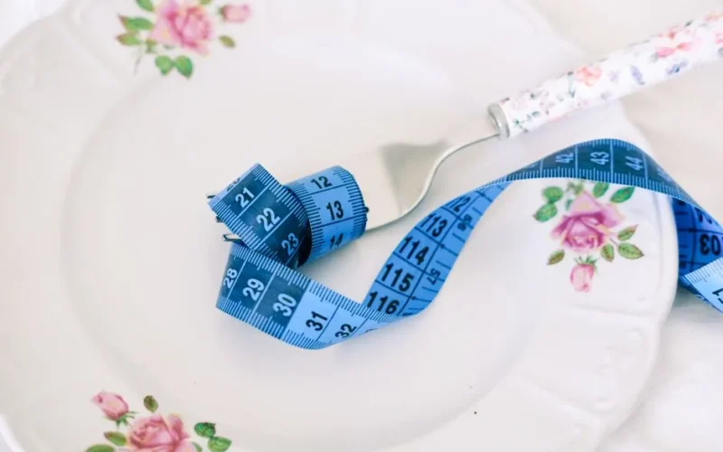 A floral plate with a fork and blue measuring tape symbolizing dieting or healthy eating.